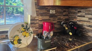 A kitchen with a marble countertop, wooden cabinets, a window with a view of greenery, and a red kettle.