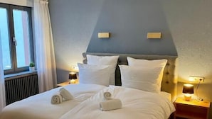 Una cama bien hecha con sábanas y toallas blancas, un cabecero de madera y lámparas de noche.