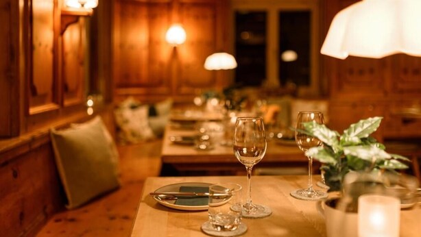 Un comedor con cálida iluminación, paneles de madera, una mesa dispuesta con platos, vasos y una vela.