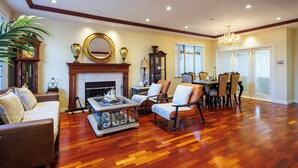 Ein geräumiges Wohnzimmer mit Holzdielen, einem Kamin, einem Essbereich mit einer Chandelier und einem großen Spiegel an der Wand.