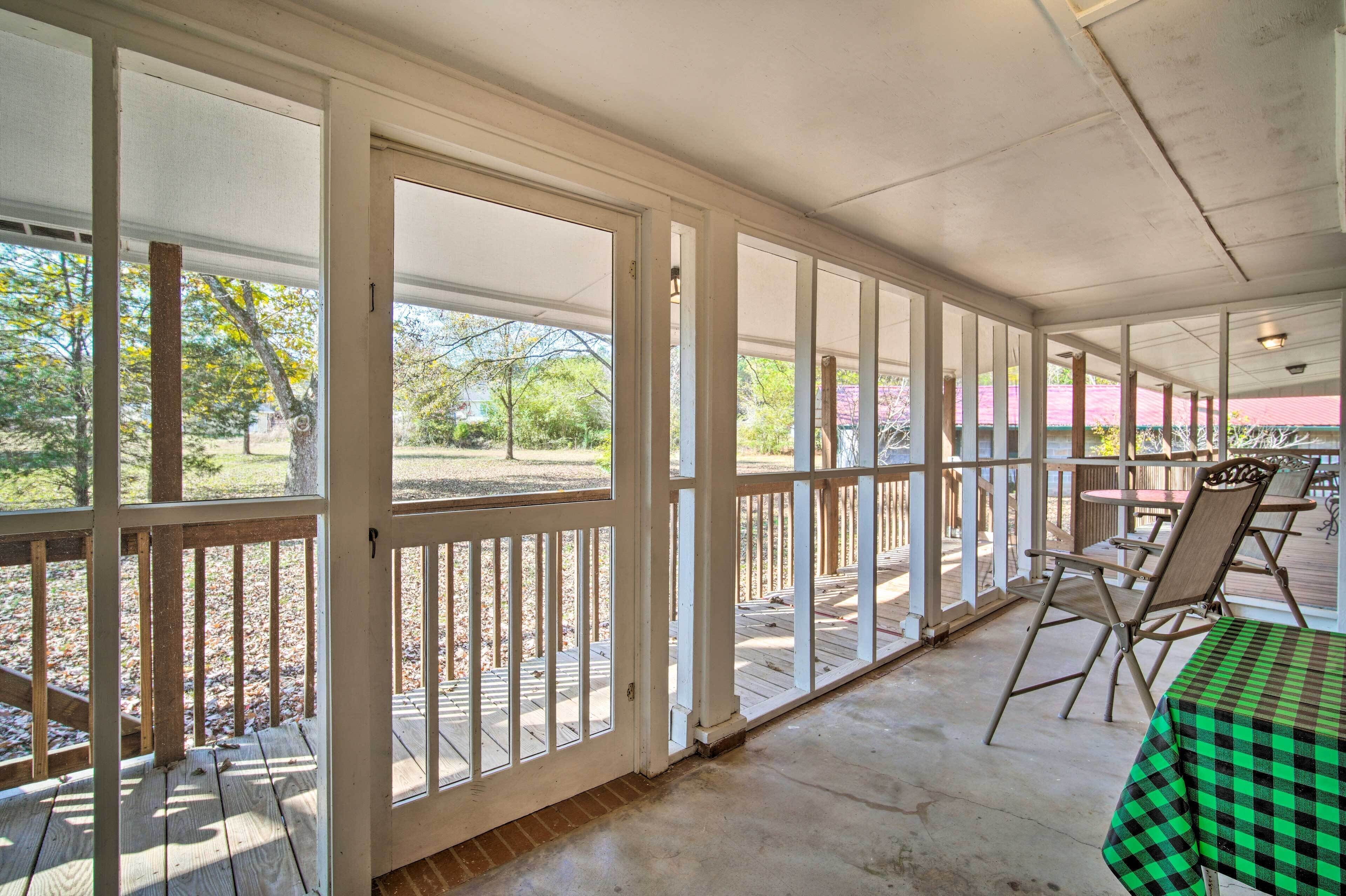A covered outdoor area with a table and chairs, large windows, and a view of the outdoors.