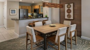 Una cocina moderna con armarios de madera, un refrigerador de acero inoxidable y una zona de comedor con mesa y sillas de madera.
