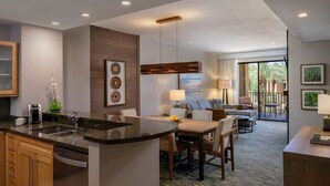 Una habitación de hotel moderna con cocina, una mesa de comedor y zona de estar con sofá y sillas.