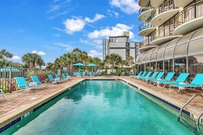 A swimming pool with lounge chairs and umbrellas, surrounded by palm trees and a modern building with balconies. - Beautiful Couples Retreat w/ Comfy King, Stunning Views & Excellent Walkability (Myrtle Beach)