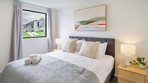 A hotel room with a large bed, a view of a modern building outside, and a painting on the wall. - City Stay, Sleeps 6 - Walk to One NZ Stadium (Christchurch)
