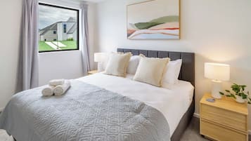 A hotel room with a large bed, a view of a modern building outside, and a painting on the wall.