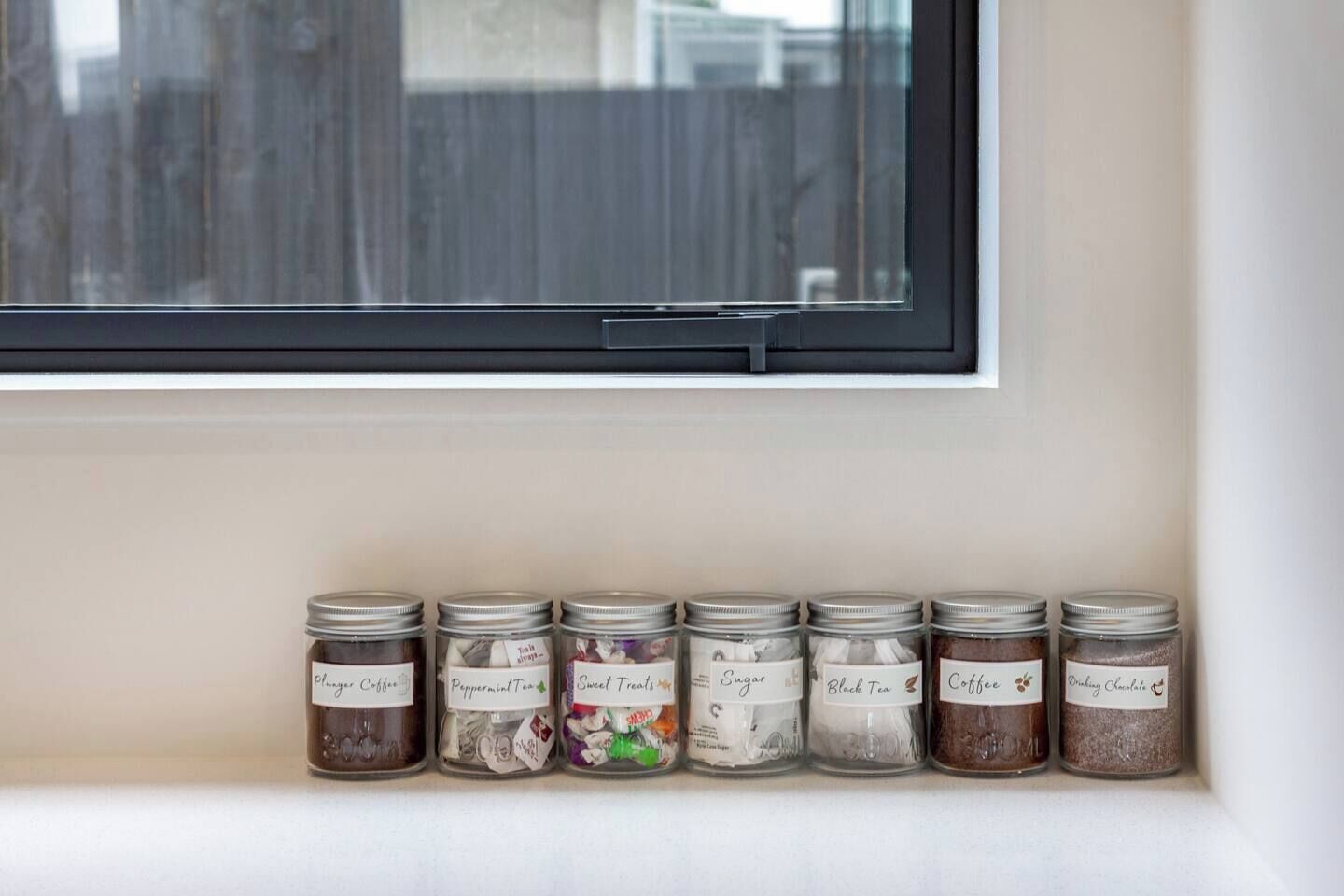 Un alféizar con siete frascos de vidrio que contienen diferentes alimentos.