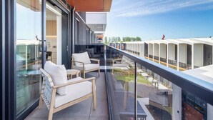 A balcony with two chairs and a table, overlooking a row of white buildings and a clear sky. - Stadium & Port Hills View 1BR Apartment | Balcony (Christchurch)