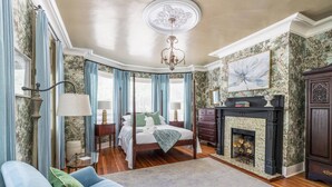 Een slaapkamer met een hemelbed, een open haard en een groot raam met gordijnen.