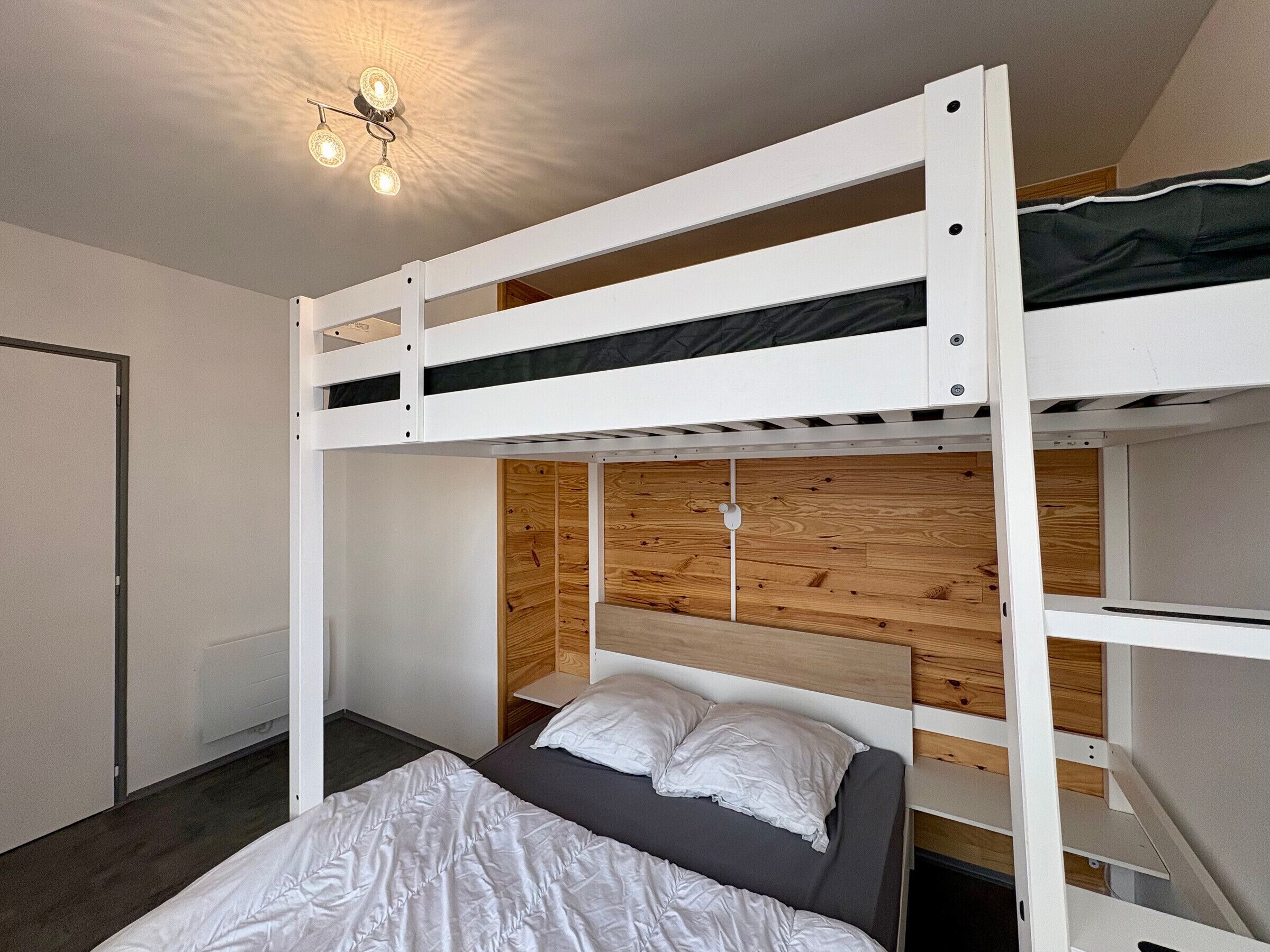 A bunk bed room with a wooden headboard, a white bed, and a ceiling light fixture.