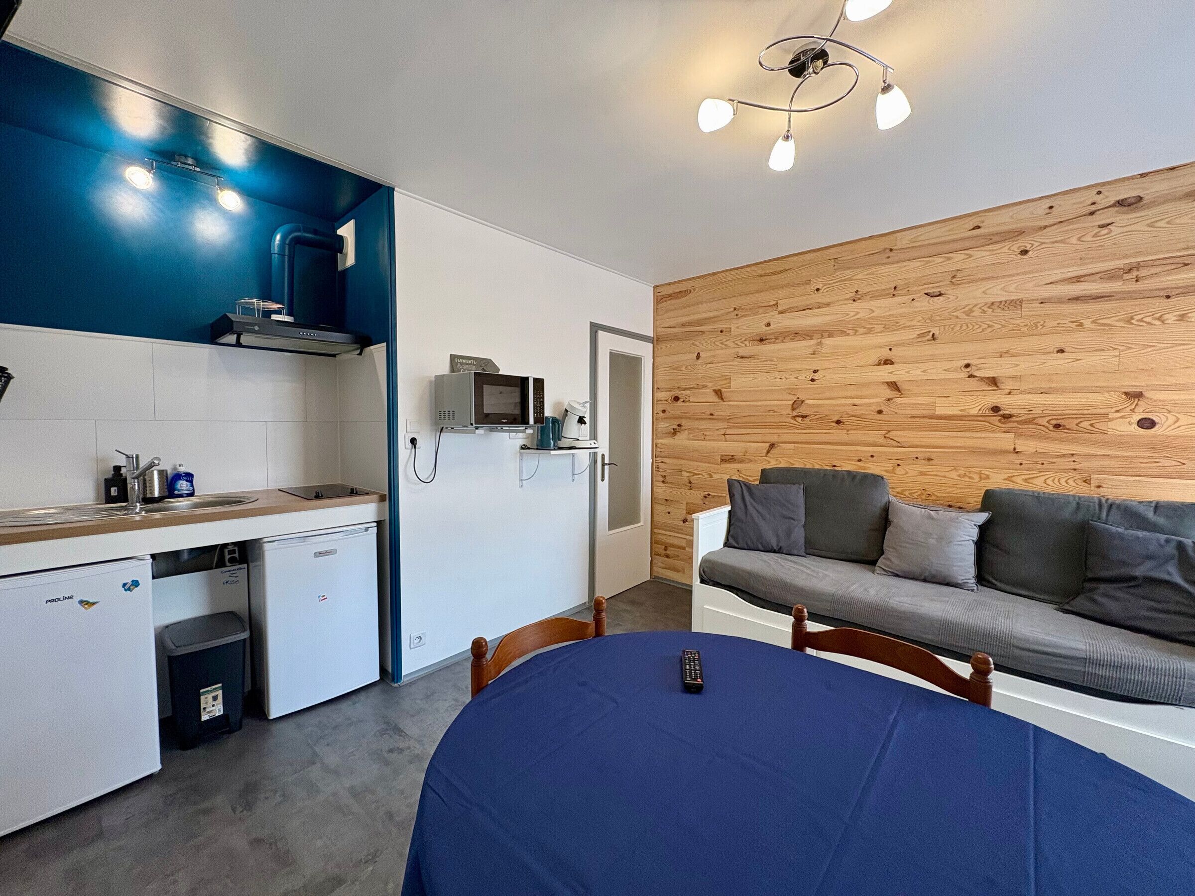 A compact kitchen with a microwave, coffee maker, and a sink. There's a dining area with a table and chairs, and a wooden wall.