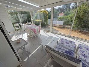 A sunlit patio with a table and chairs, a white sofa, and a view of a garden and trees. - Family house 6 pers, pets allowed, near beach (La Faute-sur-Mer)