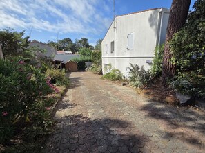 A paved pathway leading to a building with a white exterior and shutters, surrounded by greenery and trees. - Family house 6 pers, pets allowed, near beach (La Faute-sur-Mer)