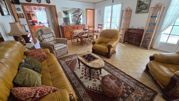 Een woonkamer met een bank, fauteuils, een salontafel, een vloerkleed en een eethoek met een tafel en stoelen.