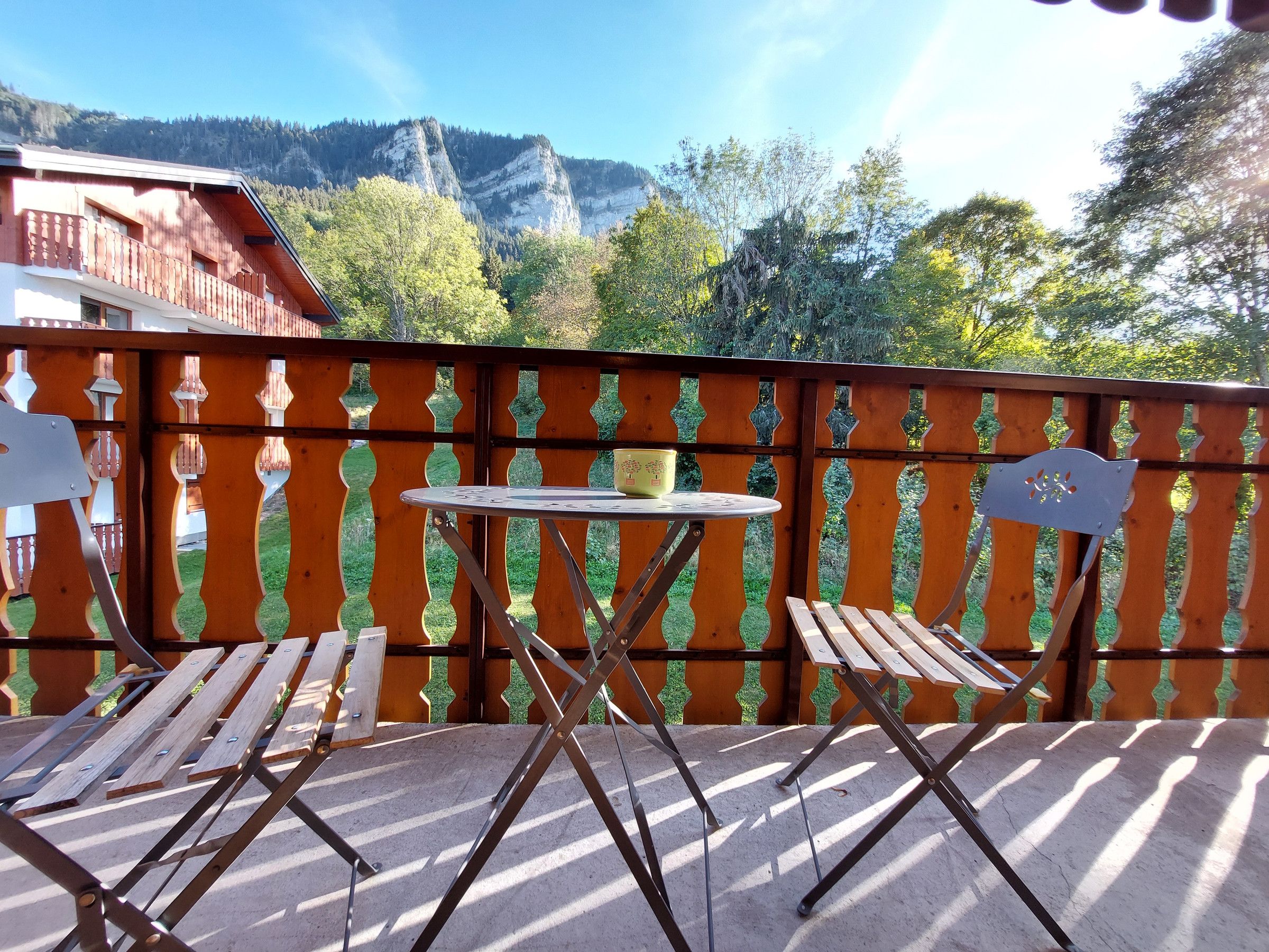 Een balkon met een tafel en stoelen, een uitzicht op bergen en een houten hek.
