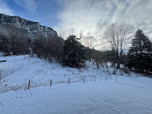 A snow-covered landscape with a mountain in the background, a fenced area, and leafless trees. - Charming apartment near slopes with parking (Thollon-les-Mémises)
