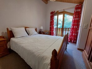 A bedroom with a wooden bed, white bedding, a nightstand with a lamp, and a window with red curtains. - Charming apartment near slopes with parking (Thollon-les-Mémises)
