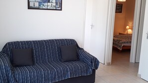 A room with a striped sofa, a framed collage of images on the wall, and a bed in the background. - Single-storey cottage near beach with parking in L'Aiguillon-sur-Mer (L'Aiguillon-sur-Mer)