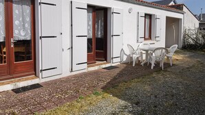 Un edificio blanco con varias puertas y ventanas, un camino de grava y un pequeño espacio al aire libre con sillas de plástico.