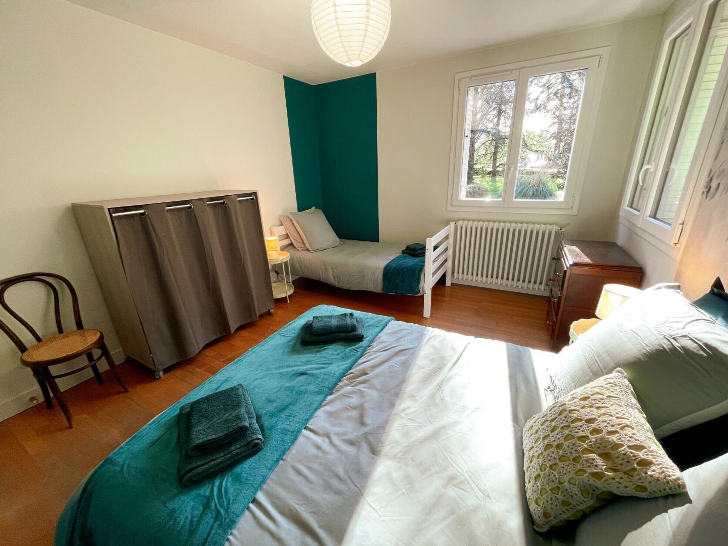 A bedroom with a bed, a chair, a wardrobe, a radiator, and a window.