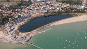 Luchtbeeld van een kustplaatsje met een jachthaven, een pier en een strand.