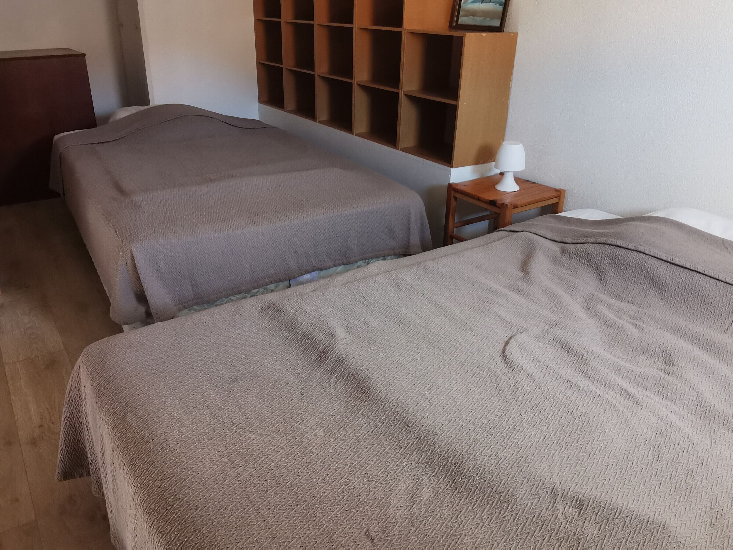 Una habitación con dos camas, una mesita de noche de madera con una lámpara y un estante en la pared con un cuadro.