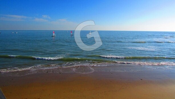 Ein Strand mit ruhigem Wasser, wolkenlosem Himmel und ein paar Segelbooten in der Ferne.