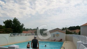 Ein Swimmingpool mit weißem Zaun, einem Rettungsschwimmer und einigen Personen im Wasser.