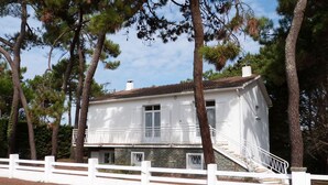 A two-story white building with a stone foundation, a white fence, and a staircase leading to the second floor. - House for 8 near beach, pets allowed (La Tranche-sur-Mer)