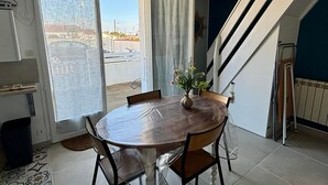 A dining area with a round table, chairs, a vase with flowers, a sliding glass door, and a view of the outside. - Cozy house for 4, near center and beach, with parking (La Tranche-sur-Mer)