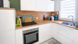 Eine moderne Küche mit weißen Schränken, einer Holzarbeitsplatte, einem eingebauten Backofen, einer Spüle und einem Fenster mit Jalousien.