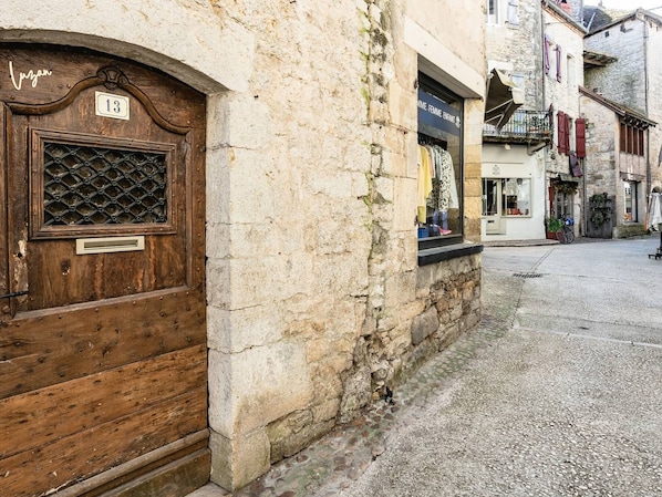 Eine schmale Gasse mit einer HolztĂŒr, die die Zahl 13 zeigt, und einem Steinhaus mit einem Schaufenster, in dem Kleidung ausgestellt ist.