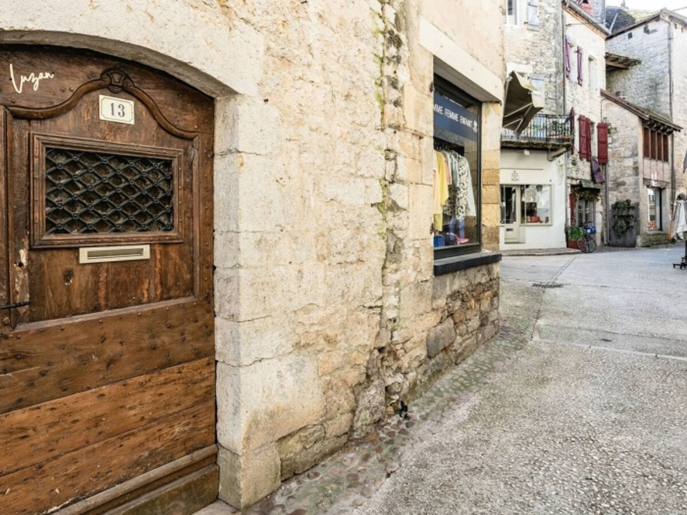 A narrow street with a wooden door labeled '13' and a stone building with a shop window.