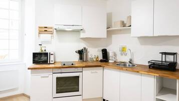 Une cuisine compacte avec des meubles blancs, un plan de travail en bois, un four encastré, un four à micro-ondes, une machine à café et un évier.