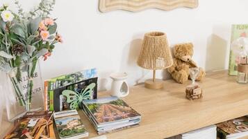 Une table en bois sur laquelle se trouve une pile de magazines, un vase avec des fleurs, une lampe, un ours en peluche et un tableau encadré accroché au mur.