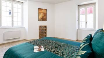 Une chambre à coucher avec un lit, une fenêtre, un radiateur et une étagère fixée au mur.