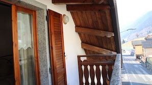 Un balcón de madera con un muro de piedra y una puerta de madera con cortina de encaje.