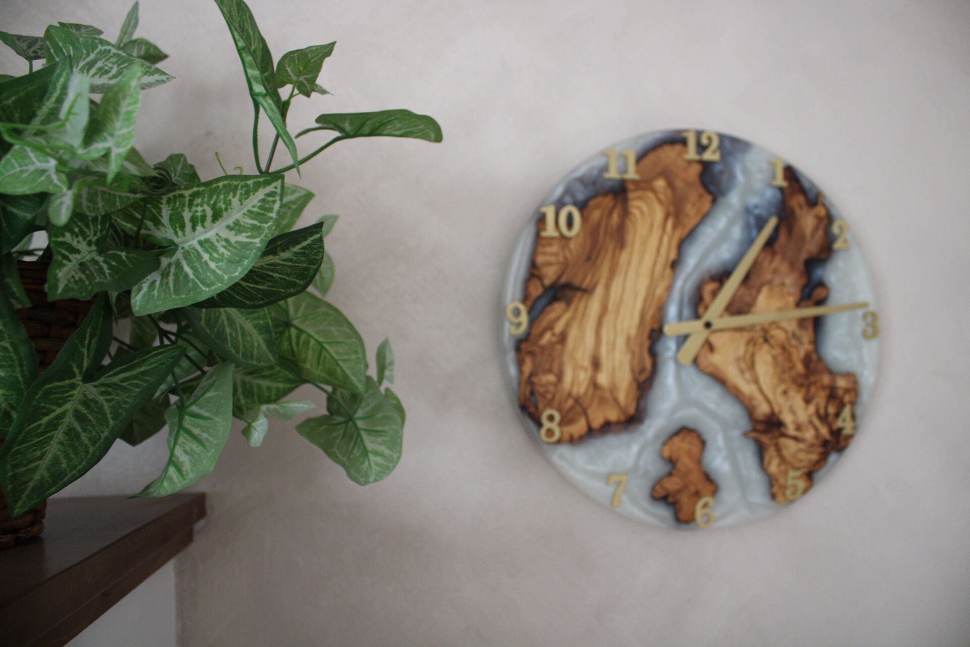 A wall clock with a wood grain design and a potted plant beside it.