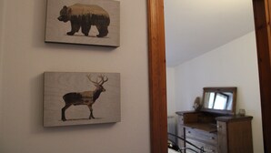 Dos grabados enmarcados de animales en una pared, un espejo que refleja una habitación con un aparador y un televisor.