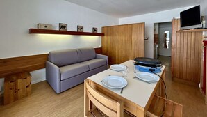 A compact living space with a sofa, dining table, and a TV mounted on a wooden cabinet. - Studio for 4 near slopes with free wifi and parking (Le Dévoluy)