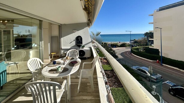 Un balcon avec une table et des chaises, donnant sur une route et une étendue d’eau.