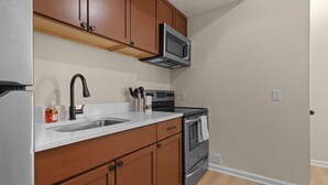 A kitchen with wooden cabinets, a stainless steel refrigerator, a microwave, a sink, and a stove.