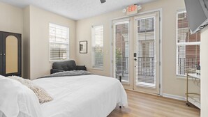 A bedroom with a bed, a ceiling fan, a door with an exit sign, and a window with blinds.