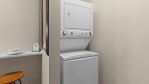 A compact laundry room with a white washer and dryer, a small table with a bowl, and a chair.
