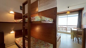 Une chambre avec un lit superposé, une échelle en bois, un bureau et un balcon avec vue.