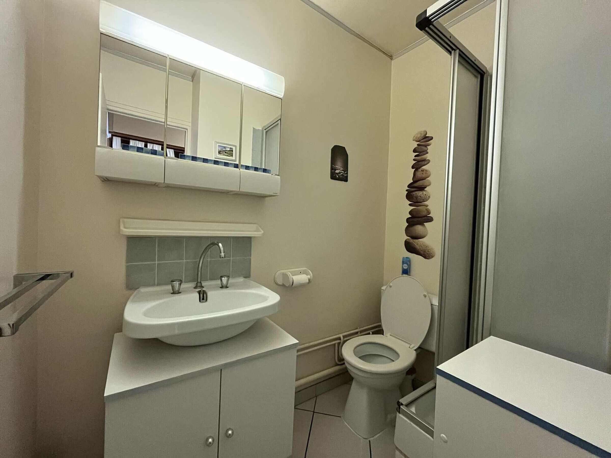 A bathroom with a sink, mirror, toilet, and a decorative stone arrangement.