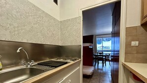 Eine moderne Küche mit Spüle aus Edelstahl, einer Holzarbeitsplatte und Blick auf einen Essbereich durch einen offenen Durchgang.