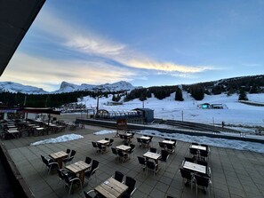 A terrace with tables and chairs, overlooking a snowy landscape with mountains and a ski slope. - Studio for 4 in SuperDévoluy with WIFI (Le Dévoluy)