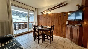 Ein Essbereich mit Tisch und Stühlen, einem Fernseher auf einer Holzkommode und Blick auf eine verschneite Landschaft durch ein großes Fenster.