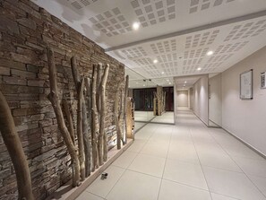 A hallway with a stone wall and wooden branches, a tiled floor, and a ceiling with recessed lighting. - Air-Conditioned 3-Room Apartment - Cavalaire-sur-Mer (Cavalaire-sur-Mer)